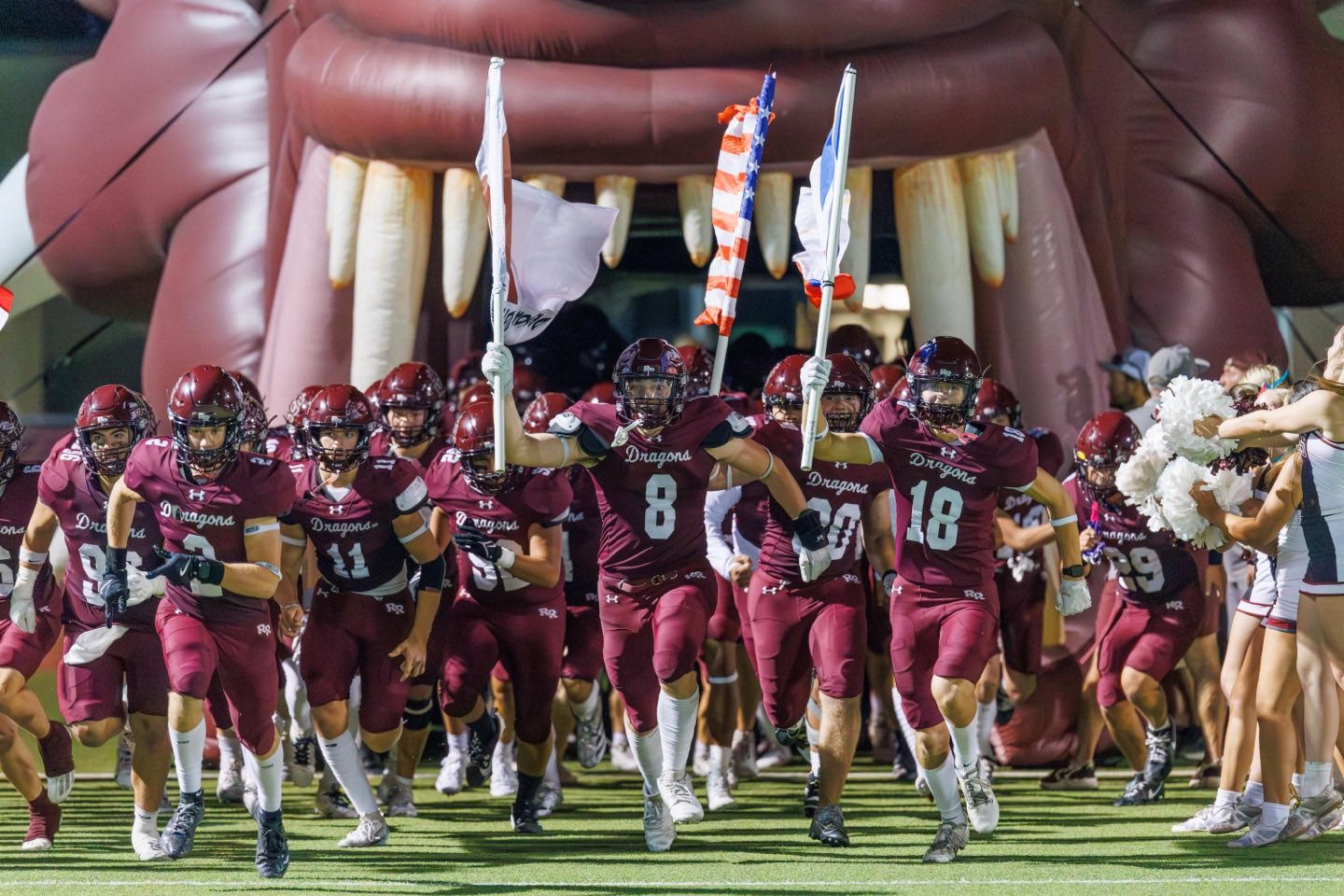 The Dragons running onto the field through the inflatable dragon tunnel, flags up, under the stadium lights.